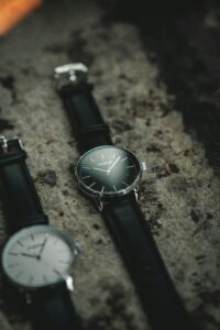 Stylish analog wristwatches with black leather straps displayed on a textured stone background.